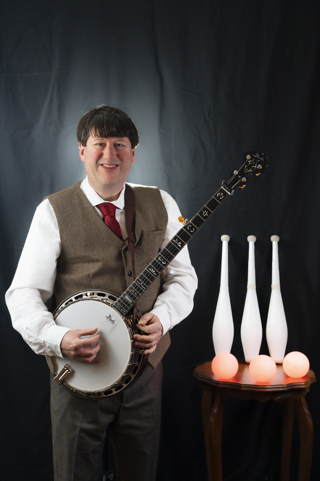 Brian Tomaszewski with banjo and juggling clubs and balls.